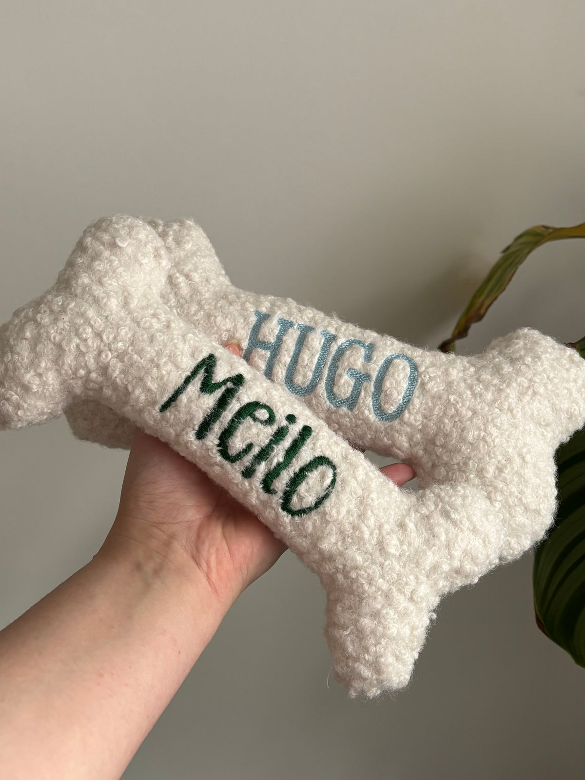 Zwei personalisierte Hundeknochen als kuscheliges Kissen. Die Knochen sind mit den Namen der Hunde bestickt.
