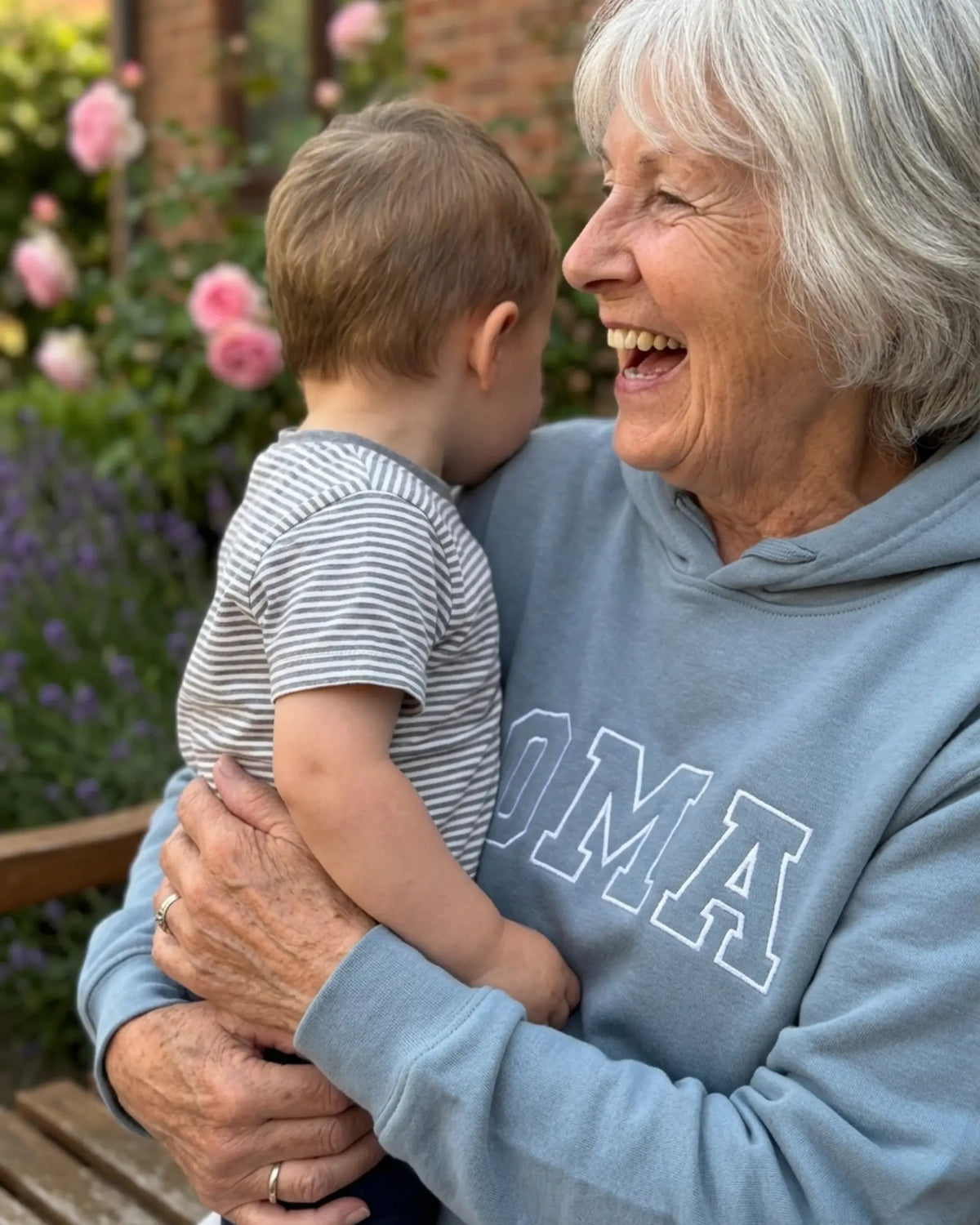 Eine Oma trägt einen personalisierten Pullover "OMA" und trägt ihren Enkel auf dem Arm. 