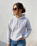 Eine Frau trägt einen Hoodie mit einem gestickten Smiley "Anti Social Club" in lila. 