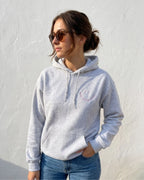 Eine Frau trägt einen Hoodie mit einem gestickten Smiley "Anti Social Club" in lila. 