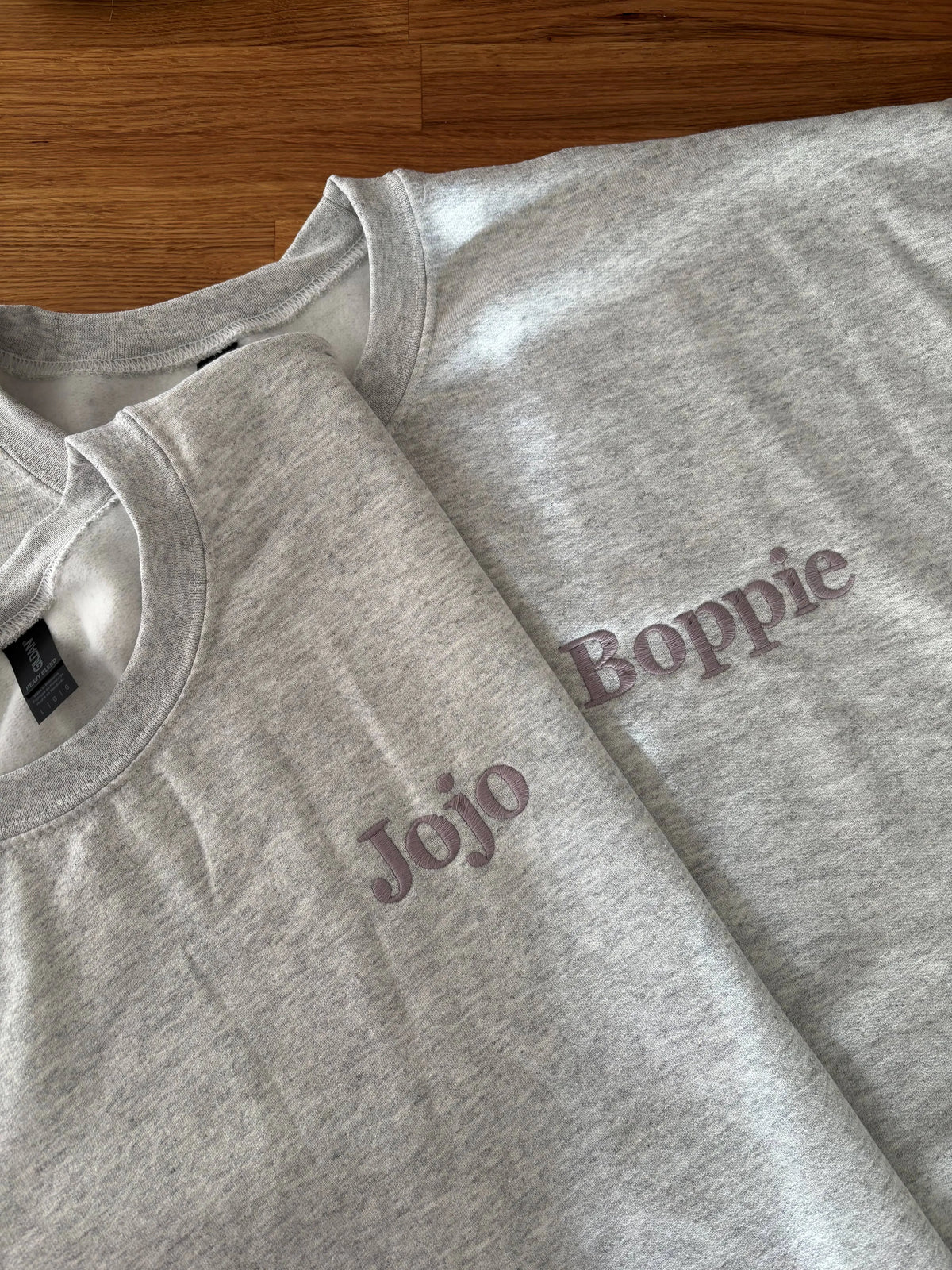 Zwei Sweater in der Farbe Ash Heather mit einer Stickerei jeweils auf der linken Brustseite: Jojo und Boppie.