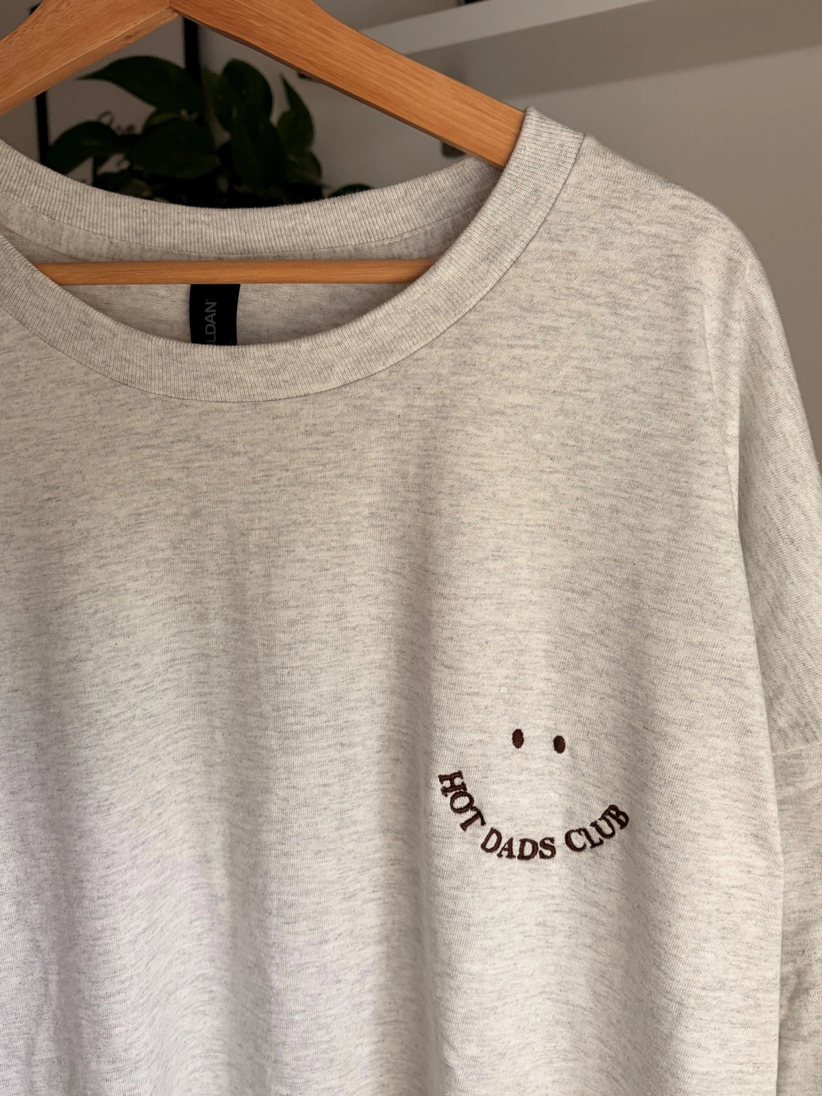 Ein T-Shirt in der Farbe Ash Heather mit einem Smiley bestickt "HOT DADS CLUB".
