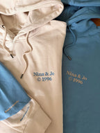 Zwei Hoodies in der Farbe Beige und Blue Dusk mit einer matching Stickerei „Nina & Jo 1996“.