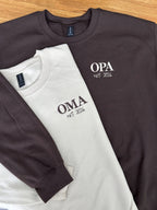 Zwei Sweater in der Farbe Beige und Dark Chocolate mit jeweils einer Stickerei in der Farbe beige und coffee brown: Oma & Opa est. 2026.