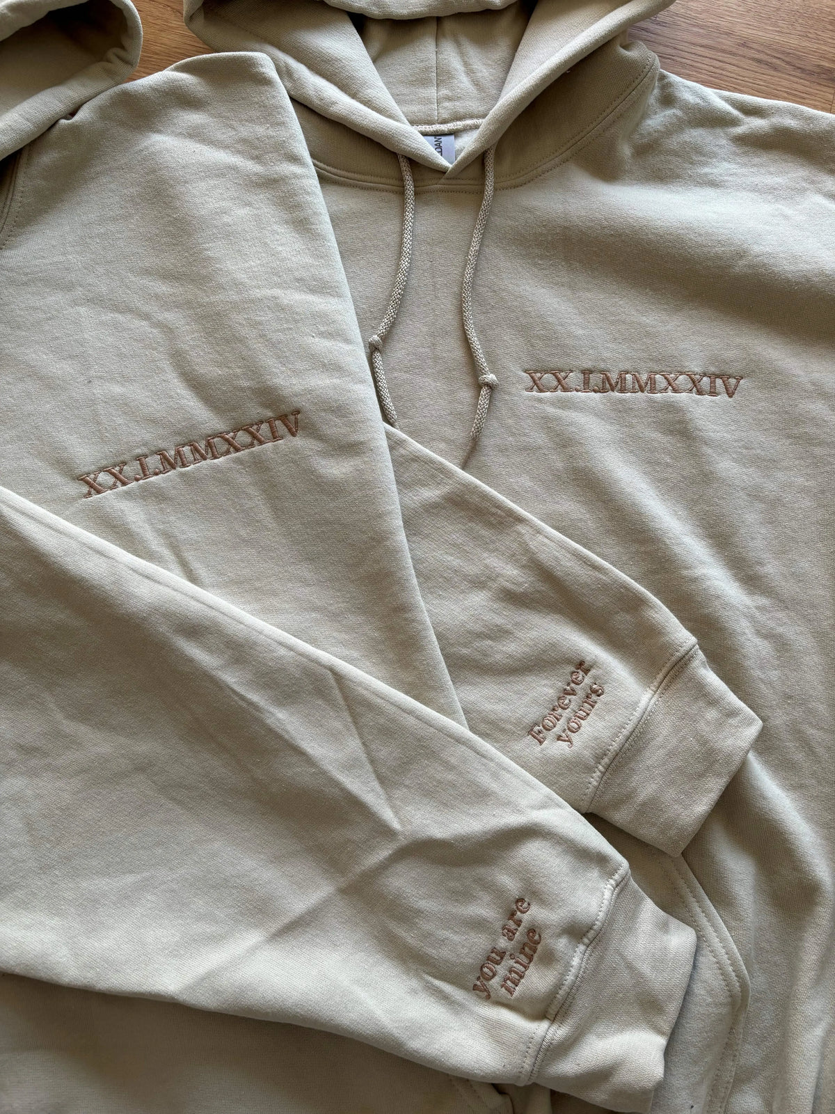 Zwei beige Hoodies mit Kapuze sind mit dem Jahrestag in rumänischen Zahlen bestickt.