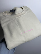 Ein beiger Sweater, wo vorne mittig ist der Satz "ceo of overhinking" in der Garnfarbe rosa gestickt ist.