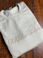 Ein Beiger Sweater mit einer beigen Stickerei auf der Brust "Godmother".