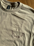 Beiges T-Shirt mit Rundhalsausschnitt. Das Shirt hat ein gesticktes Smiley-Gesicht und die Worte "COOL AUNTS CLUB" in einem geschwungenen Design. Der Text und das Smiley-Gesicht sind in verschiedenen Farben.