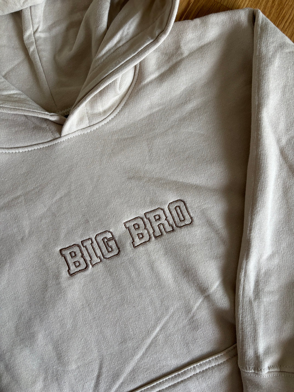 Ein beiger Pullover mit Kapuze mit einem Stick vorne BIG BRO in braun.