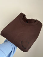 Ein Sweater in der Farbe Dark Chocolate mit einer Stickerei in schwarz vorne links auf der Brust, die wie ein Smiley aussieht: Hot Moms Club. 
