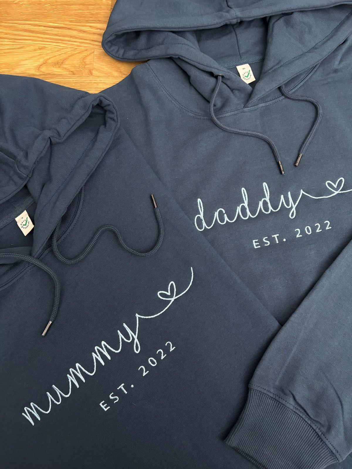 Zwei Hoodies in der Farbe Navy Blue mit einer weißen Stickerei vorne mittig: mummy und Daddy est 2022.