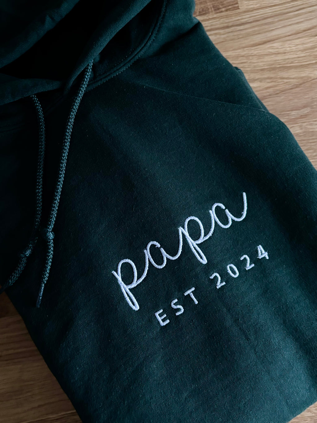 Ein personalisierter Pullover mit Kapuze. Auf der Brust ist in weiß "Papa est. 2024" gestickt.