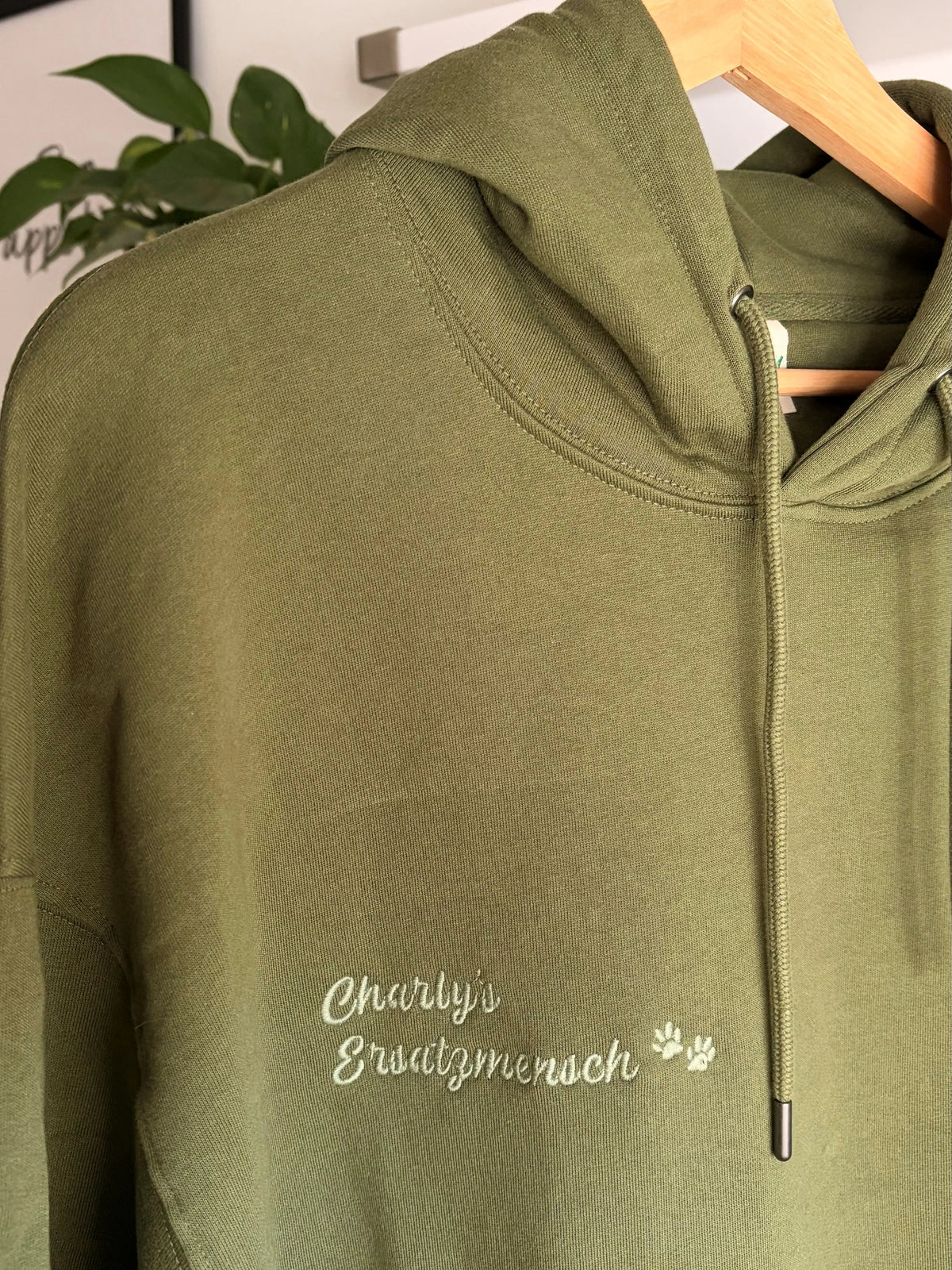 Der Pullover in der Farbe Forest Green ist mit einem grünen Garn bestickt. Auf dem Pullover steht Charly‘s Ersatzmensch mit zwei Hundepfoten.