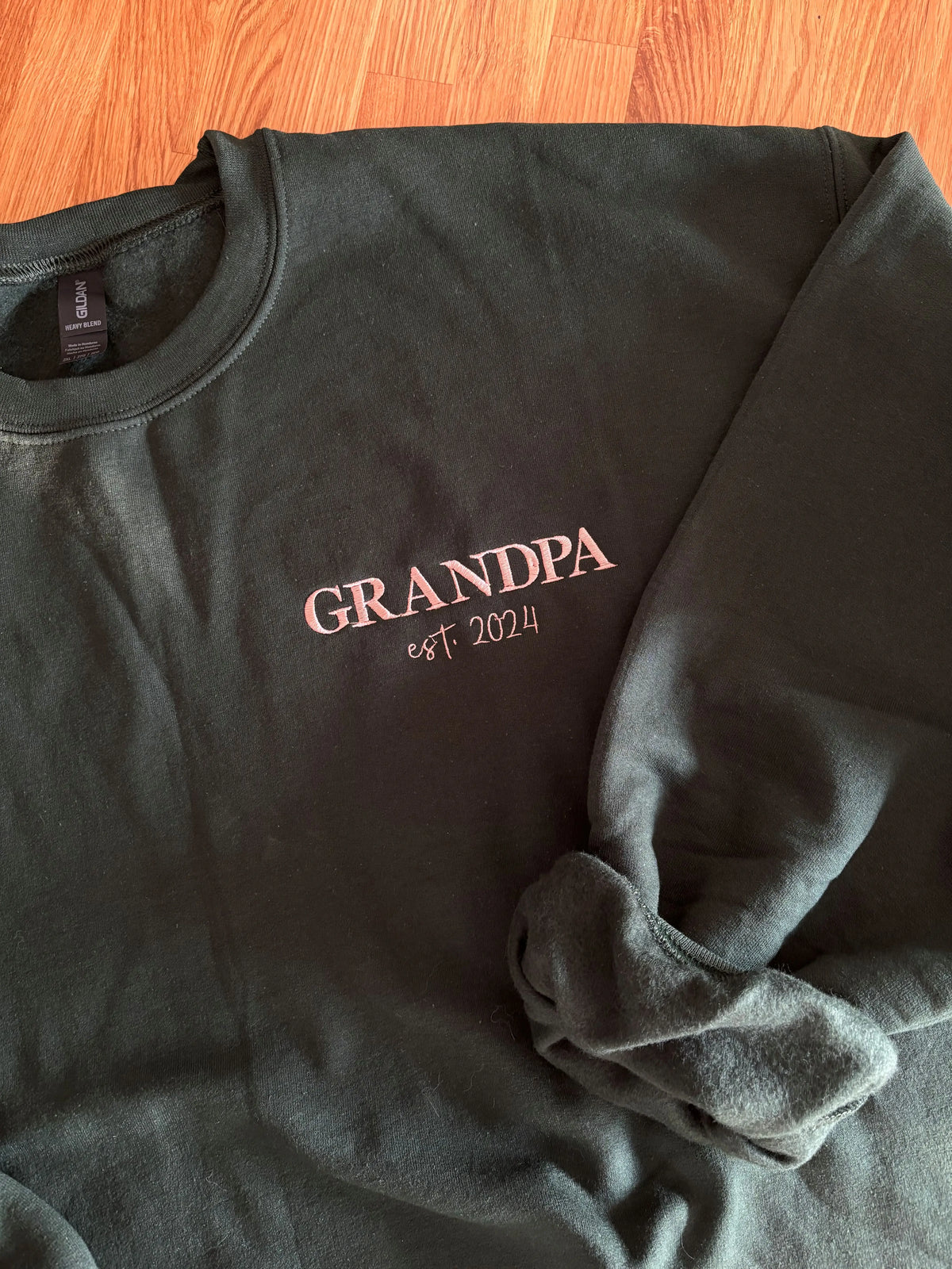 Ein Sweater in der Farbe Forest Green mit einer Stickerei in der Farbe beige: Grandpa est. 2024. 
