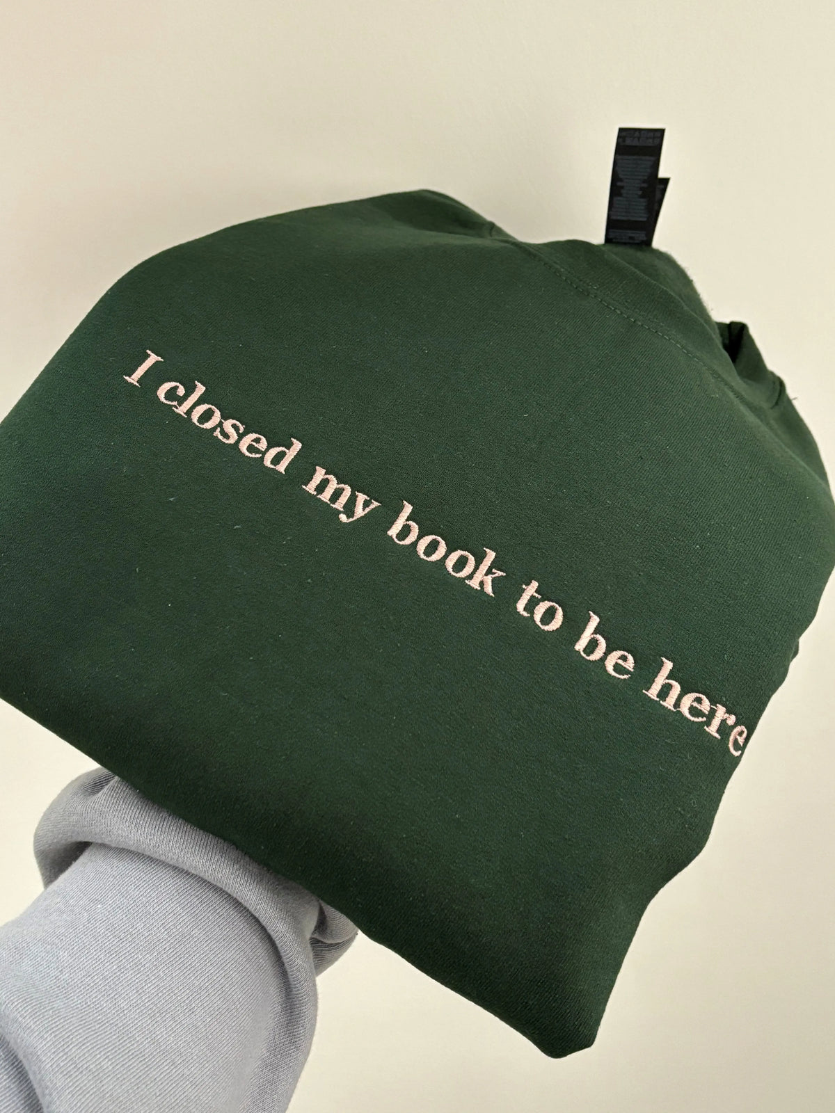 Ein Pullover in der Farbe Forest Green mit dem Schriftzug I closed my Book To be Here. Der Sweater ist mit einem dunkel beigen Garn bestickt.