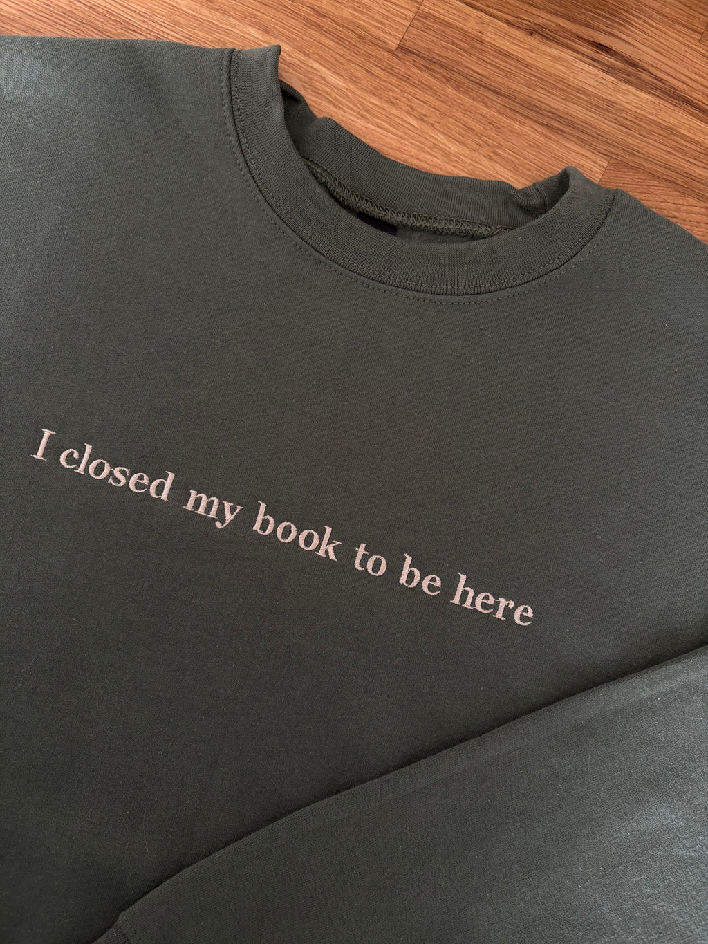 Ein grüner Sweater mit einem beigen Stick. Der Pullover liegt auf einem Holztisch.