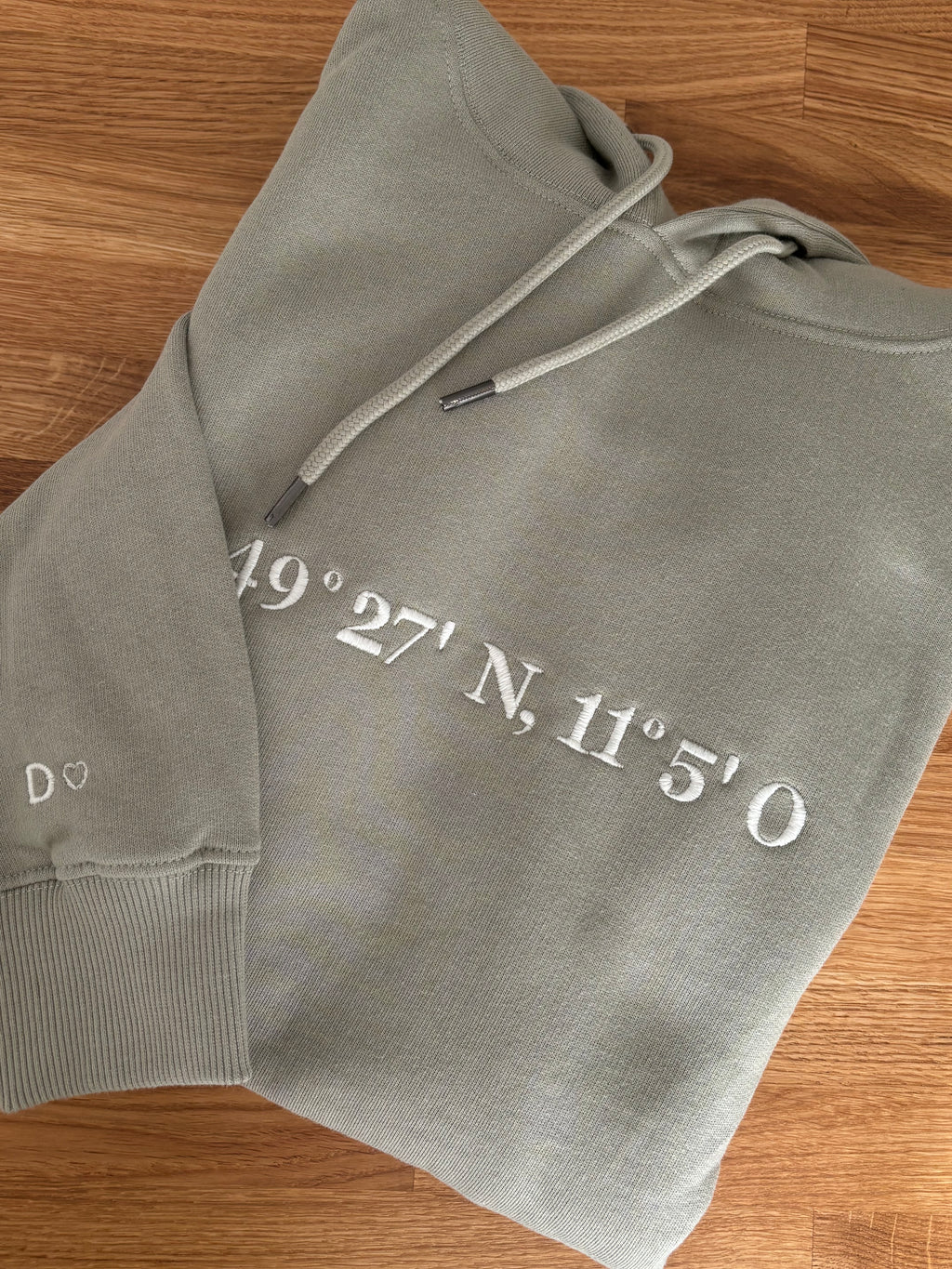 Der Ultra Heavy Pullover ist Pistazien grün und mit einem weißen Garn bestickt. Auf dem Pullover ist der erste Teil der Koordinaten gestickt. Auf einem zweiten Pullover ist der andere Teil.