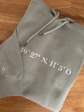 Der Ultra Heavy Pullover ist Pistazien grün und mit einem weißen Garn bestickt. Auf dem Pullover ist der erste Teil der Koordinaten gestickt. Auf einem zweiten Pullover ist der andere Teil.