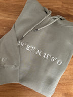 Der Ultra Heavy Pullover ist Pistazien grün und mit einem weißen Garn bestickt. Auf dem Pullover ist der erste Teil der Koordinaten gestickt. Auf einem zweiten Pullover ist der andere Teil.