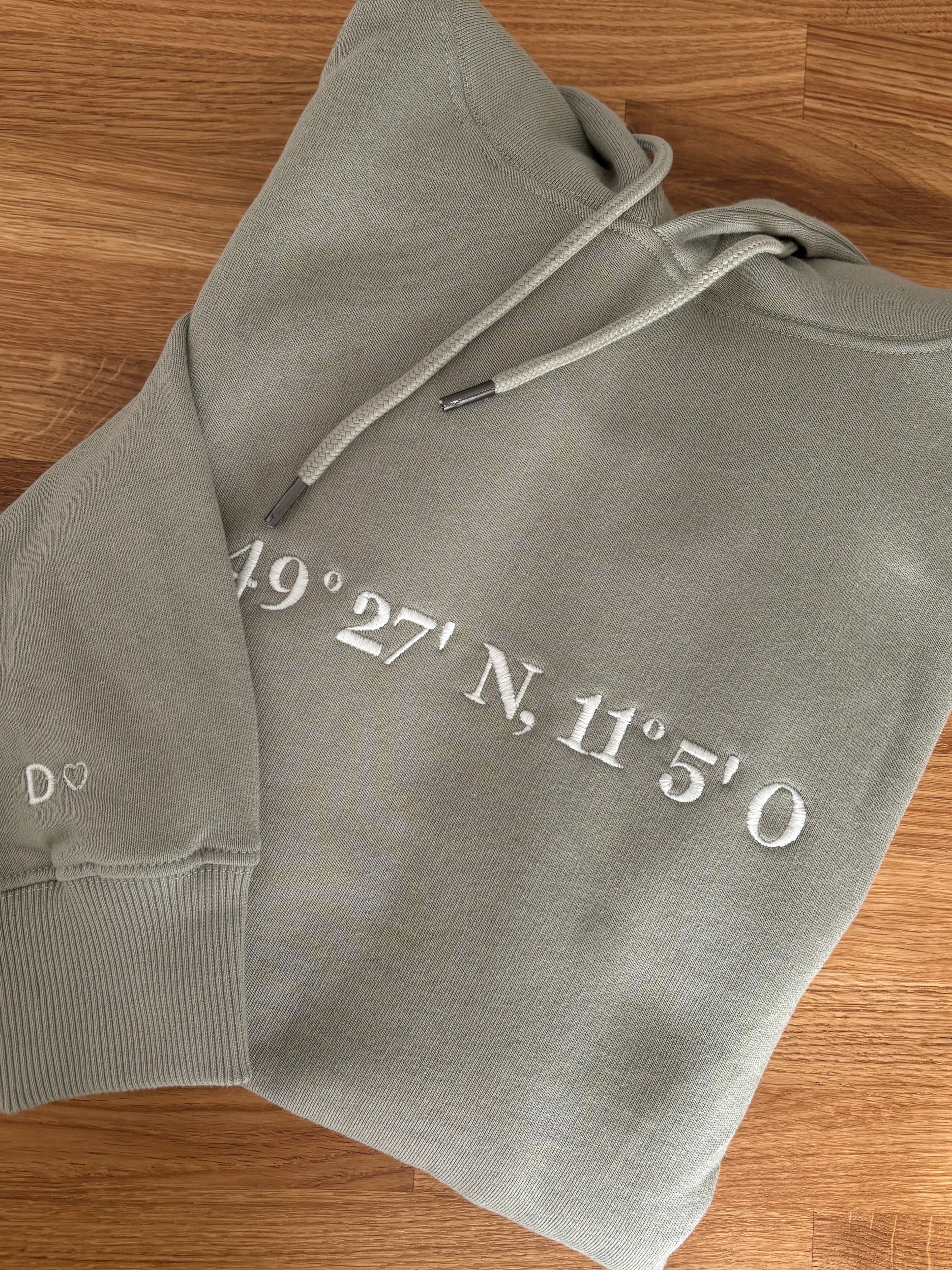 Der Ultra Heavy Pullover ist Pistazien grün und mit einem weißen Garn bestickt. Auf dem Pullover ist der erste Teil der Koordinaten gestickt. Auf einem zweiten Pullover ist der andere Teil.