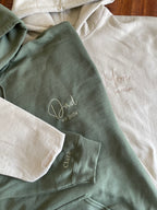 Zwei personalisierte und bestickte Hoodies mit Kapuze, worauf Mom und Dad stehen. Außerdem ist noch das Jahr, in dem sie Eltern geworden sind, gestickt. Am Ärmel ist der Name der gemeinsamen Tochter gestickt.