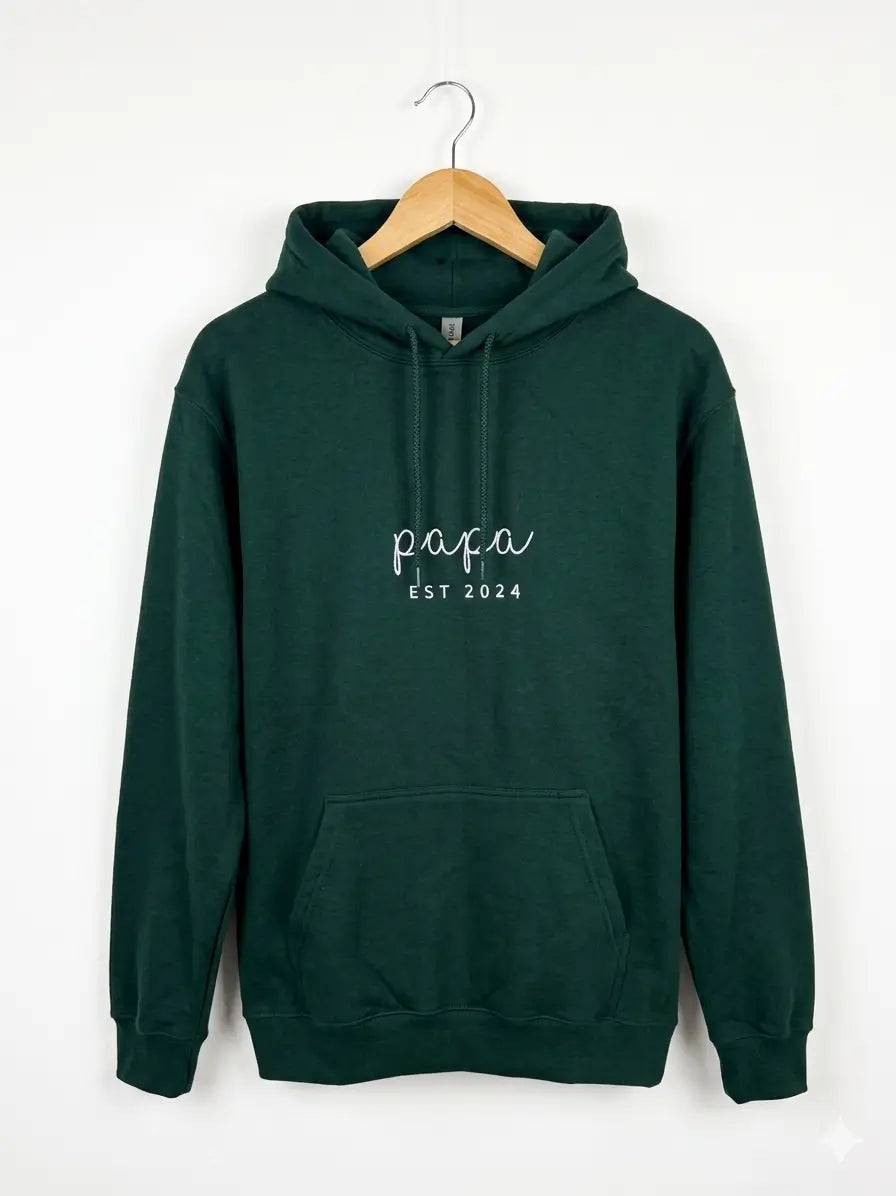 Ein Hoodie in der Farbe Forest Green mit einer personalisierten Stickerei vorne auf der Brust: papa est 2024.