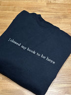 Ein schwarzer Hoodie mit einem grauen Stick auf der Brust "I closed my book to be here".