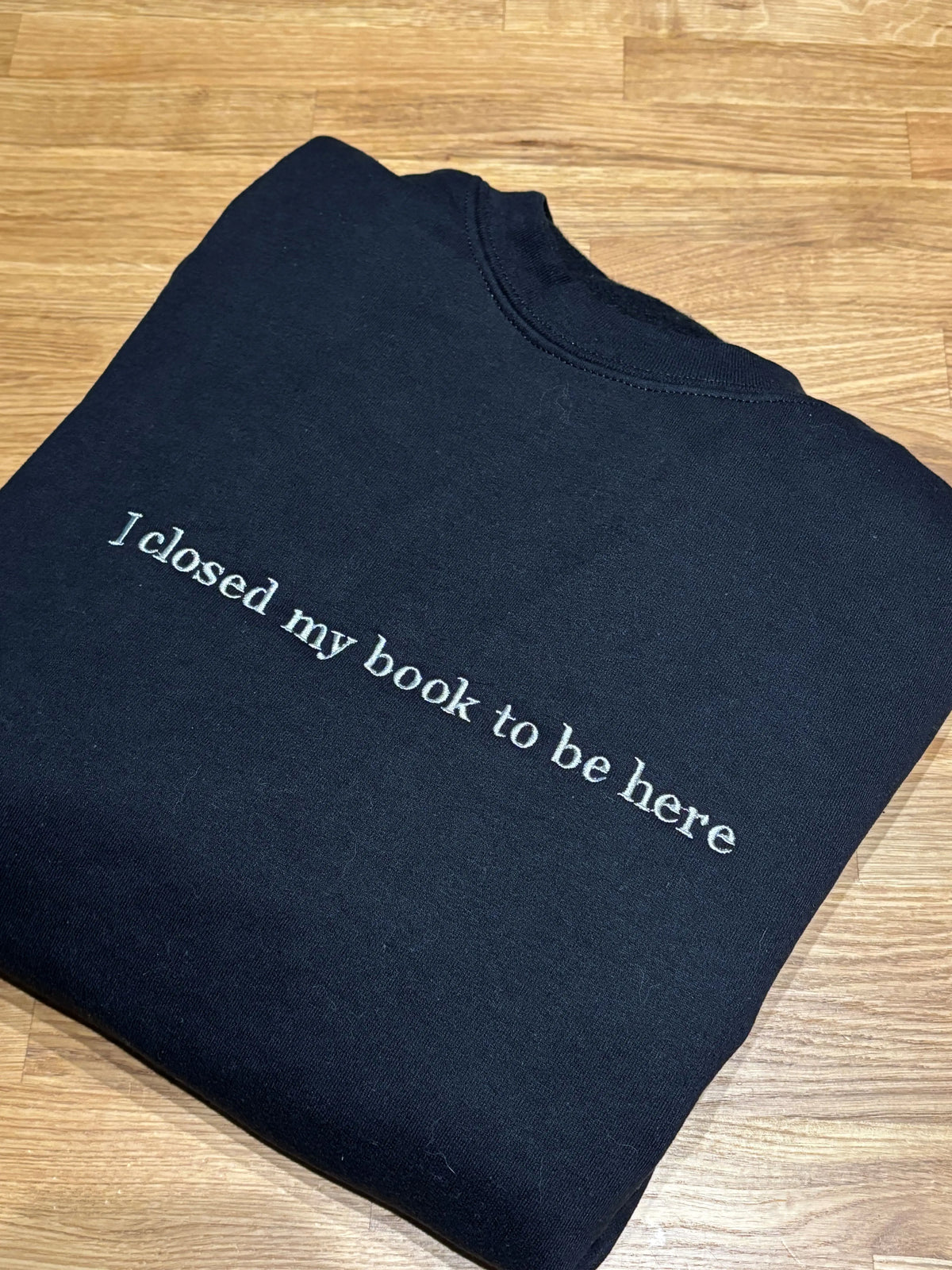 Ein schwarzer Hoodie mit einem grauen Stick auf der Brust "I closed my book to be here".