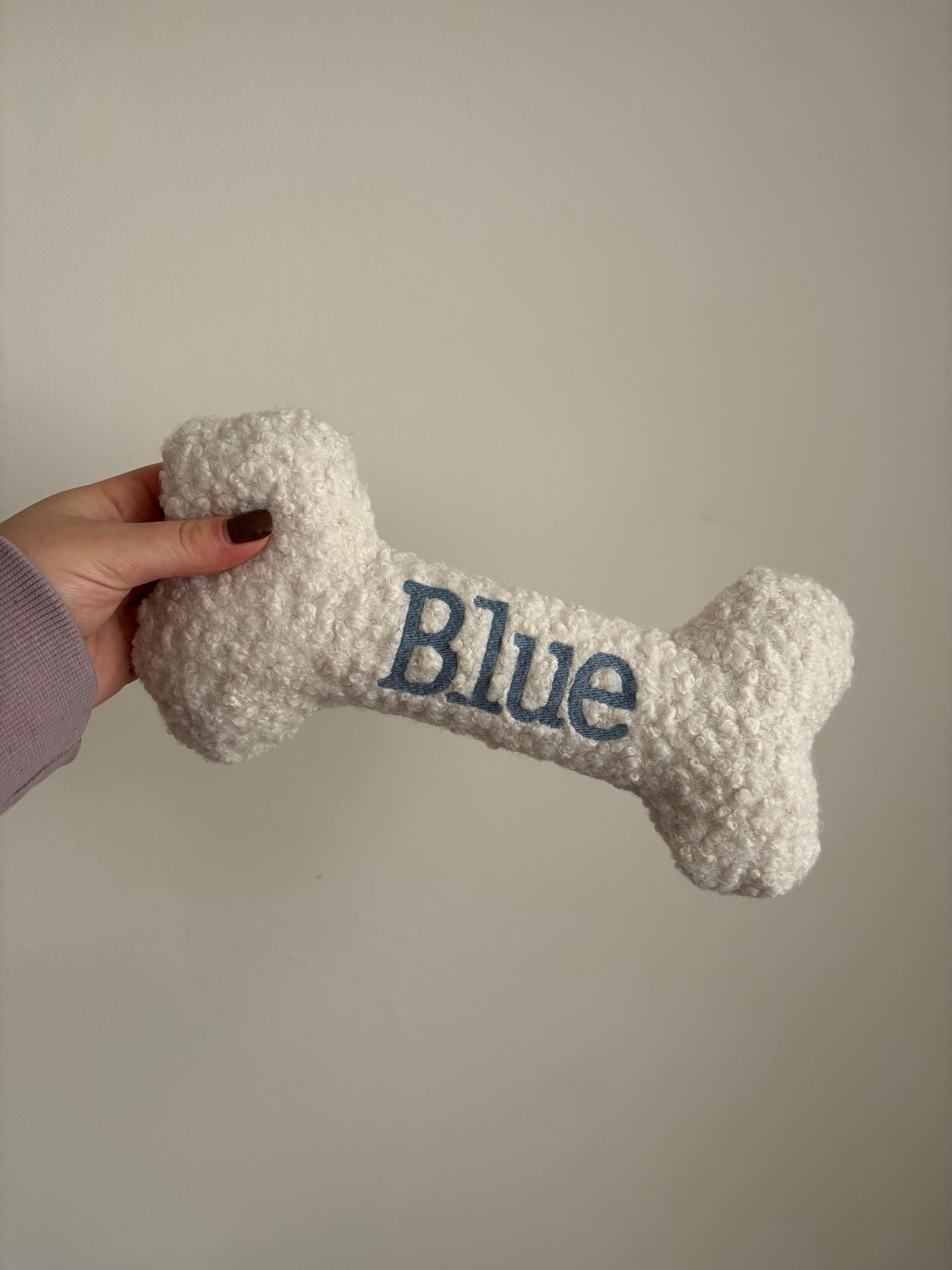Ein großer personalisierte Hundeknochen als kuscheliges Kissen. Der Knochen ist mit dem Namen des Hundes Blue bestickt.
