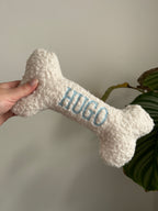 Ein großer personalisierte Hundeknochen als kuscheliges Kissen. Der Knochen ist mit dem Namen des Hundes Hugo bestickt.