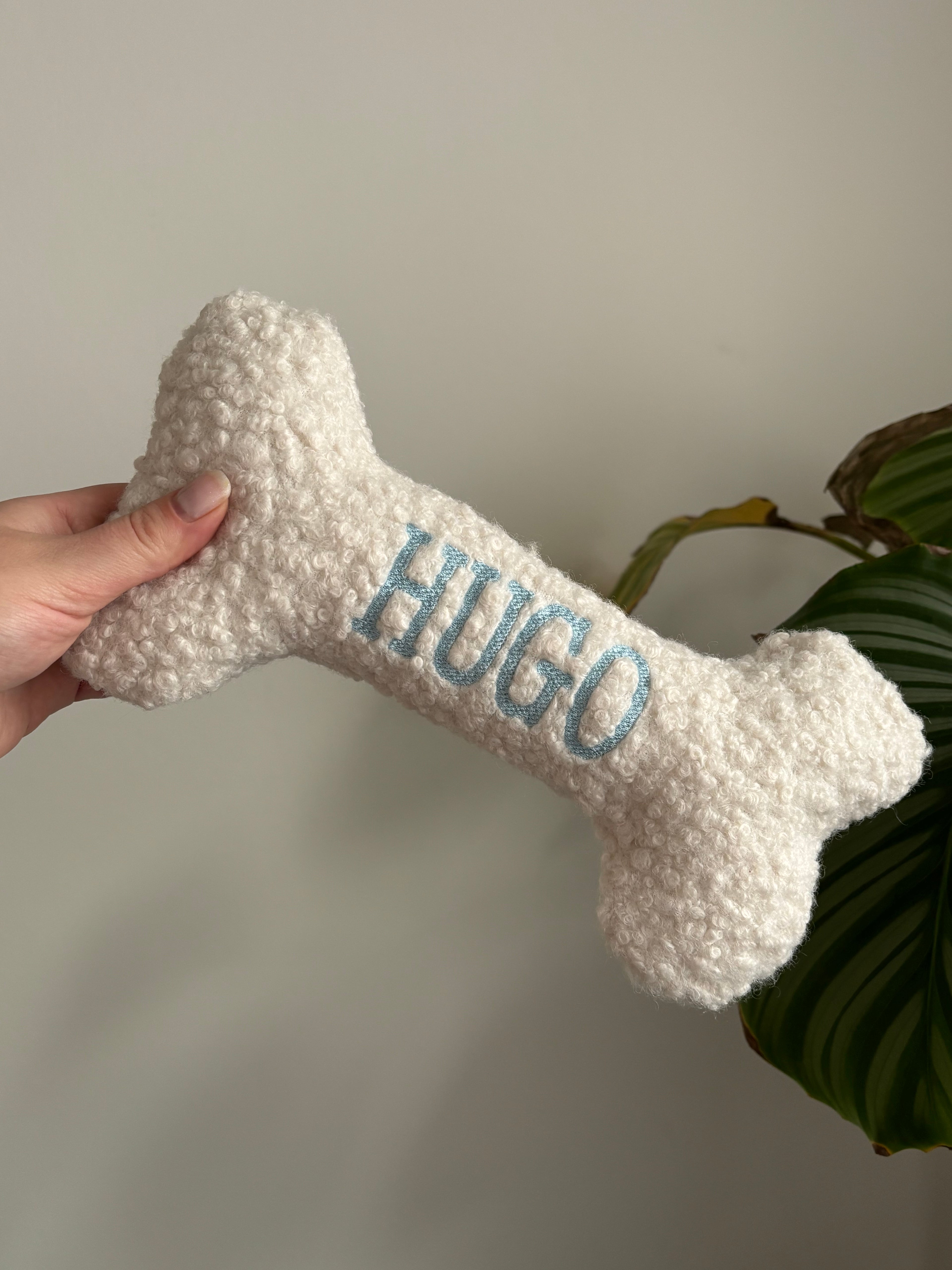 Ein großer personalisierte Hundeknochen als kuscheliges Kissen. Der Knochen ist mit dem Namen des Hundes Hugo bestickt.