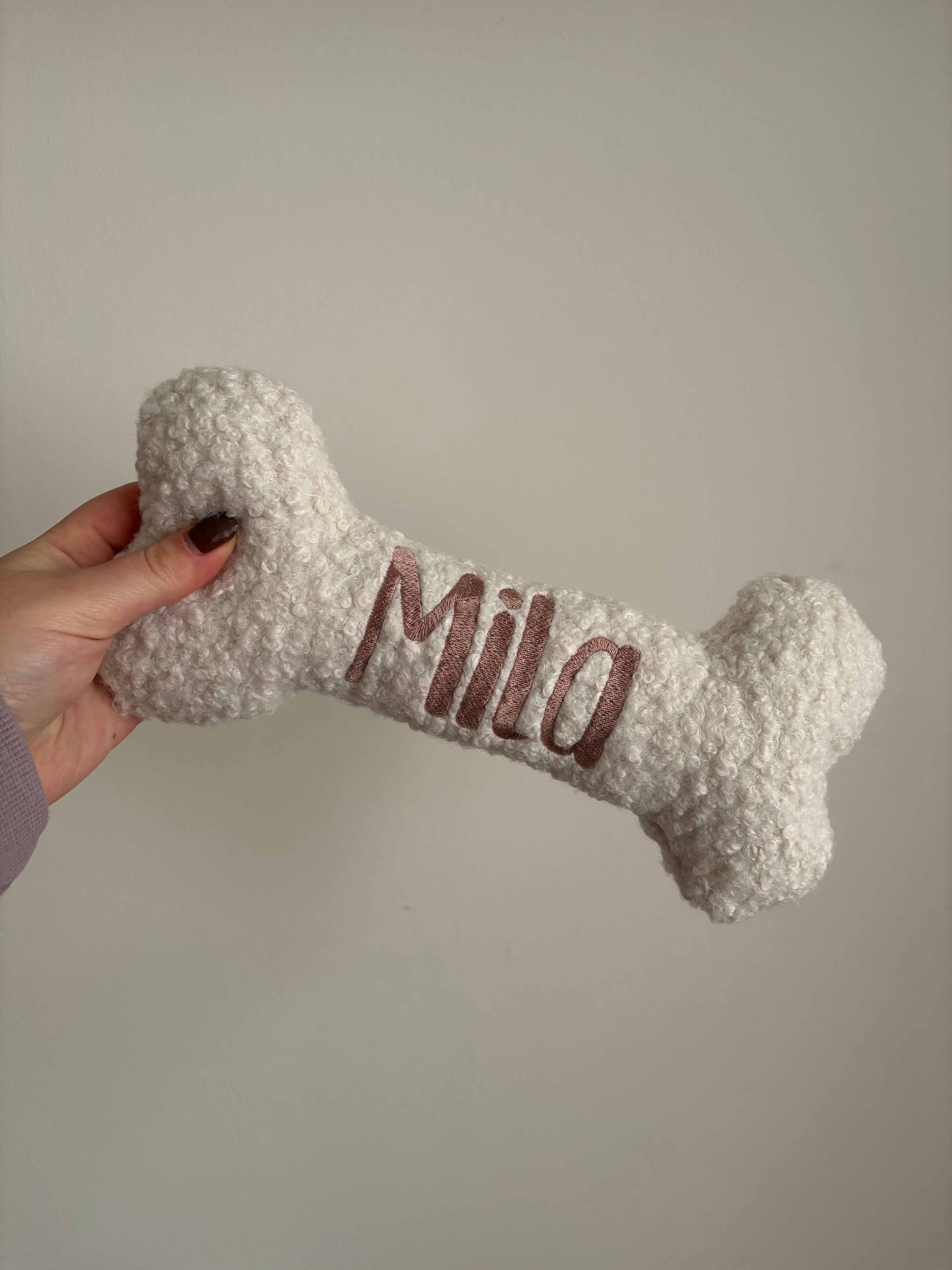 Ein großer personalisierte Hundeknochen als kuscheliges Kissen. Der Knochen ist mit dem Namen des verstorbenen Hundes Mila bestickt.