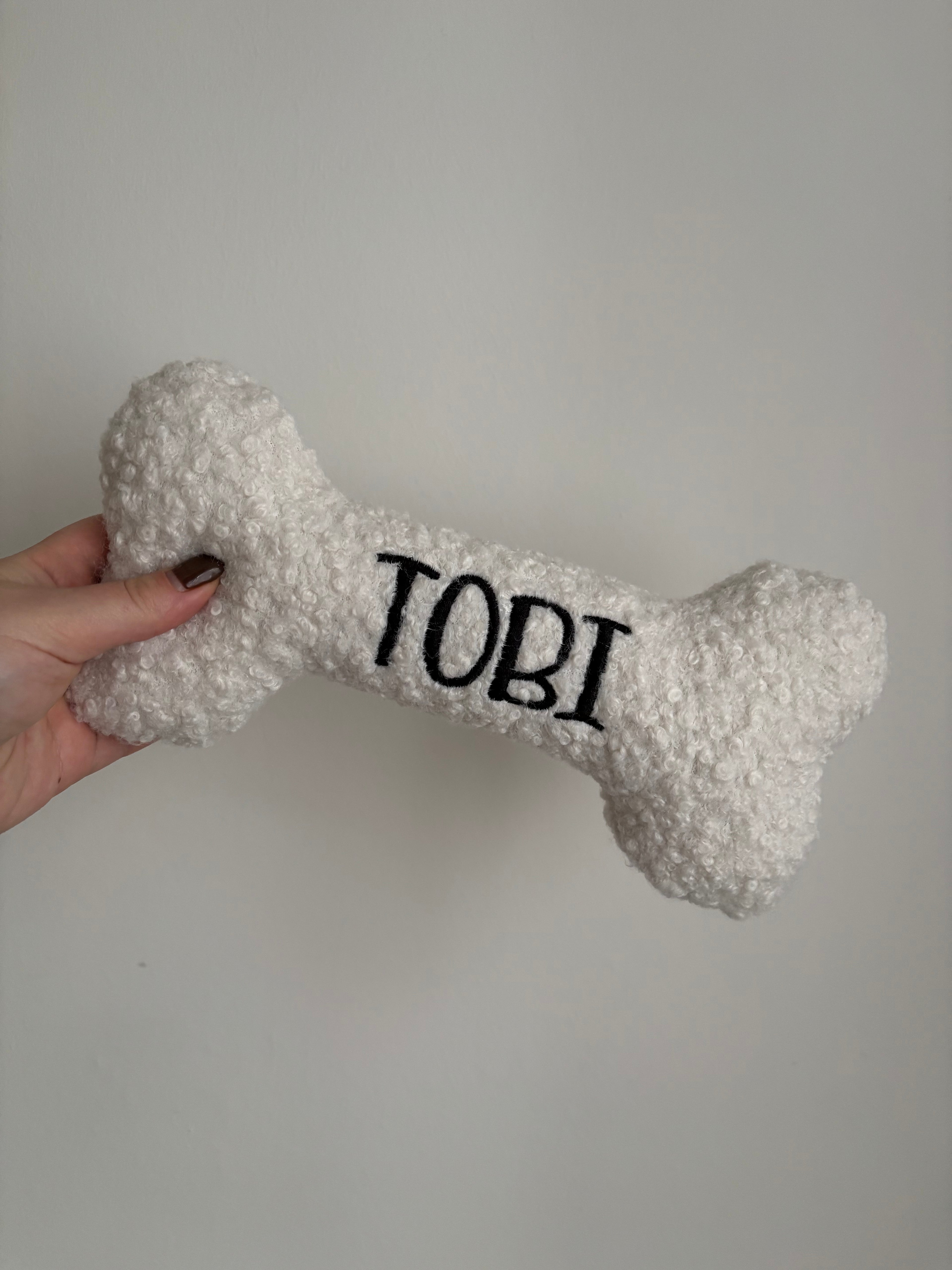 Ein großer personalisierte Hundeknochen als kuscheliges Kissen. Der Knochen ist mit dem Namen des Hundes Tobi bestickt.