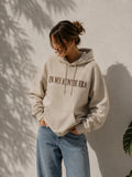Eine Frau trägt einen personalisierten beigen Hoodie mit der Stickerei vorne "IN MY AUNTIE ERA".