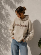 Eine Frau trägt einen personalisierten beigen Hoodie mit der Stickerei vorne "IN MY AUNTIE ERA".