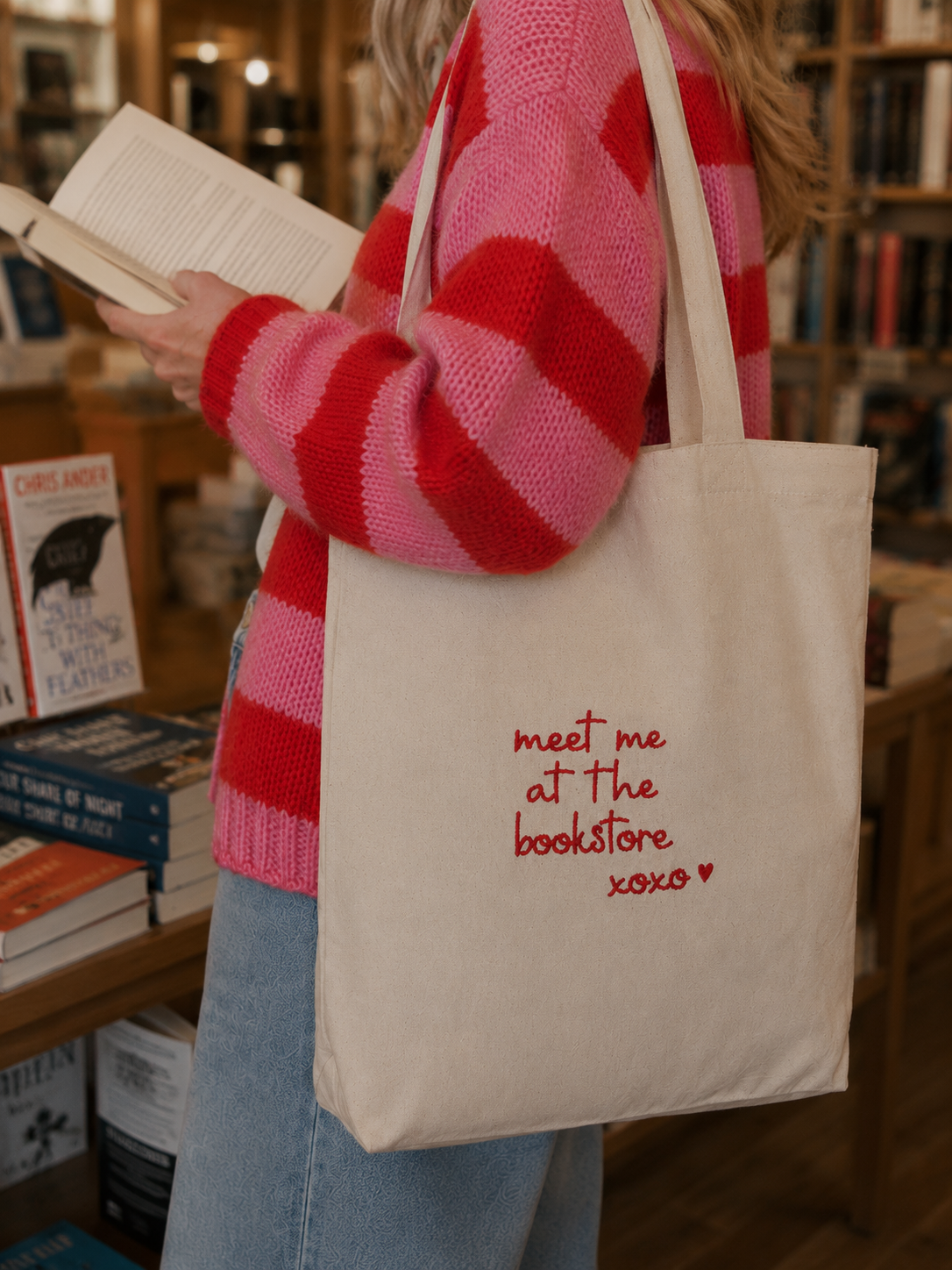Nahaufnahme eines cremefarbenen Jutebeutels mit roter Stickerei in einer warm beleuchteten Buchhandlung.