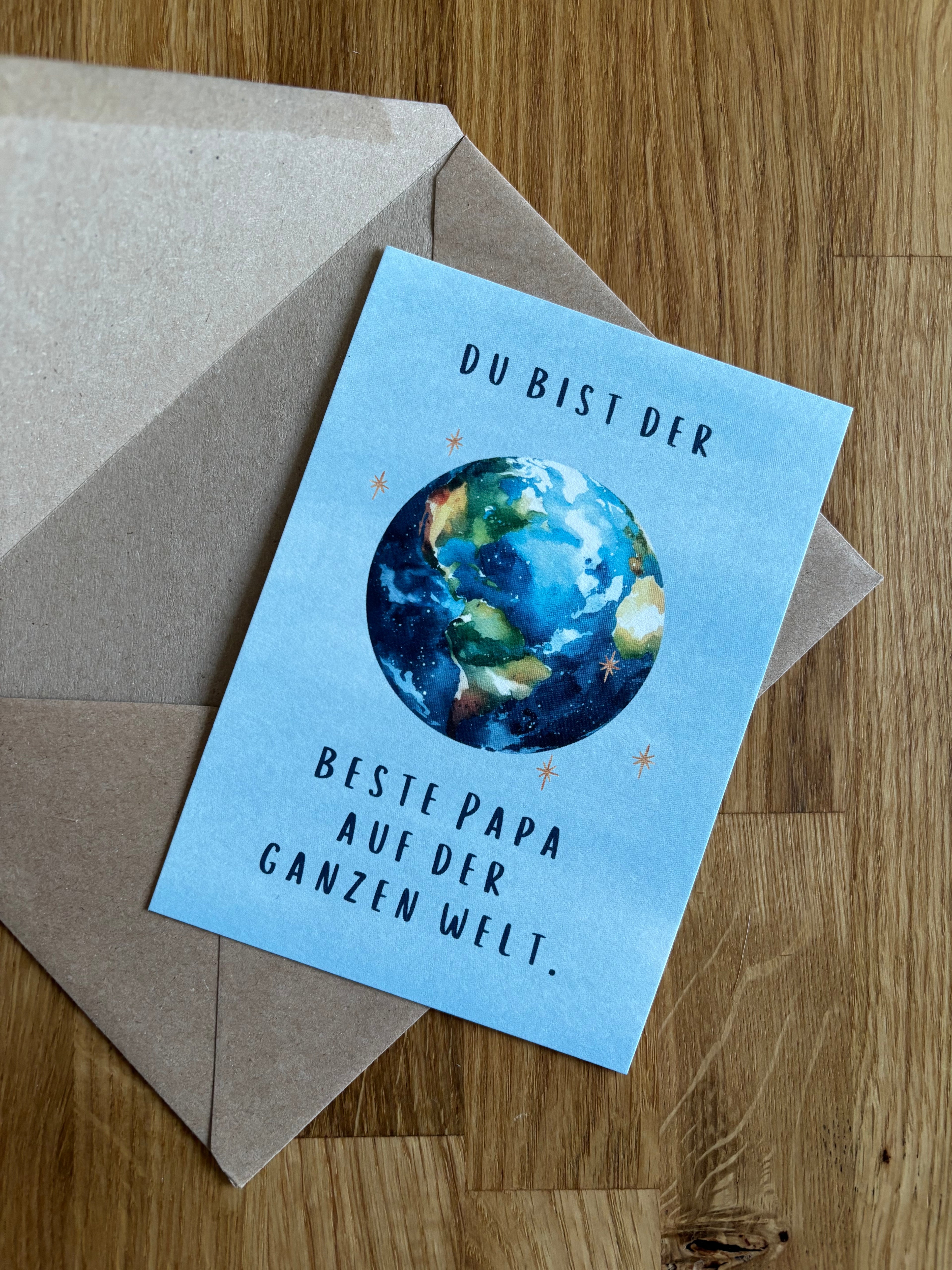 Eine blaue Postkarte "Du bist der beste Papa auf der ganzen Welt" mit einer Weltkugel.