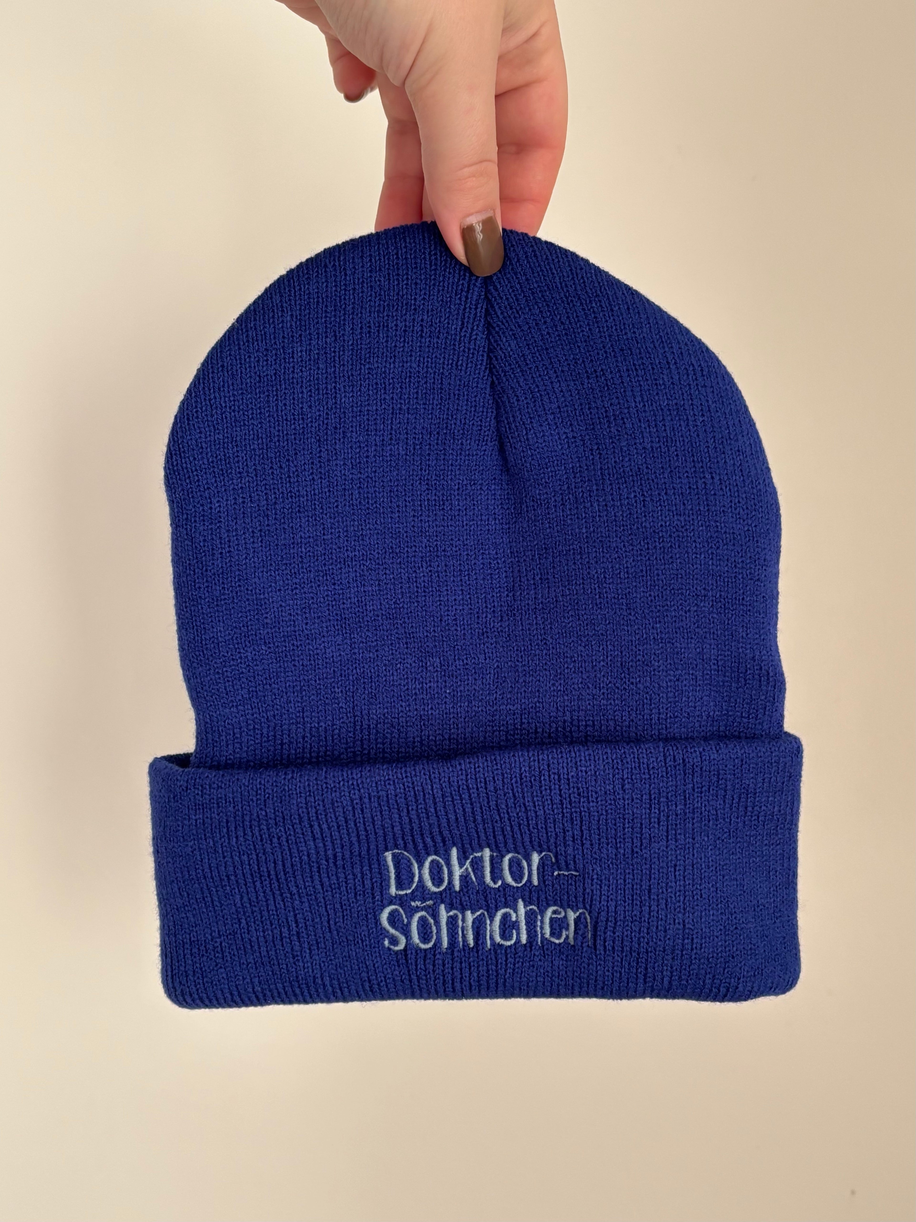 Eine Kindermütze in der Farbe Royal Blue mit einer Stickerei vorne in Stone Blue: Doktor-Söhnchen.