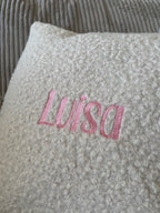 Ein besticktes Kissen mit einem Rosa Stick Luisa. 