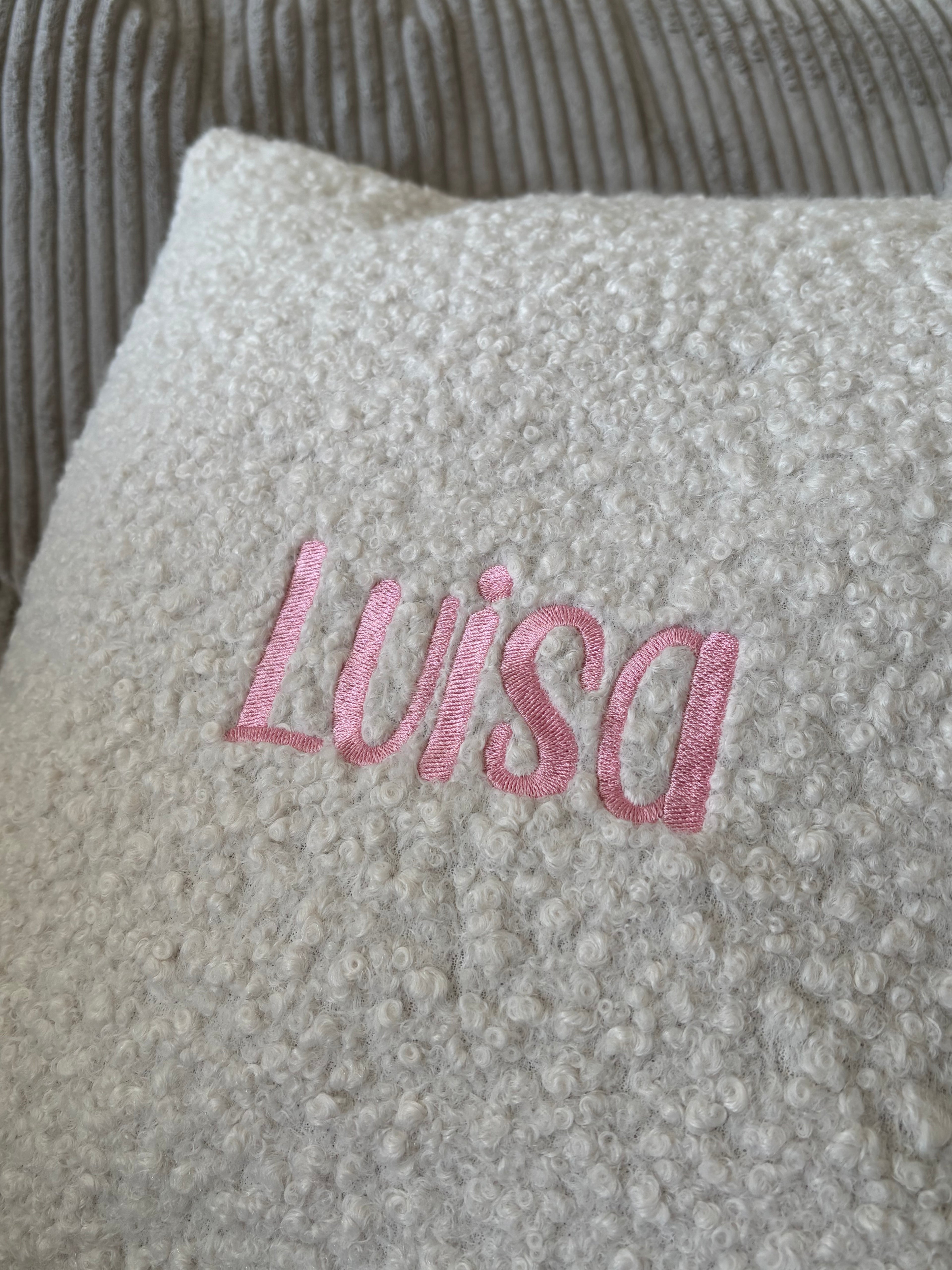 Ein besticktes Kissen mit einem Rosa Stick Luisa. 