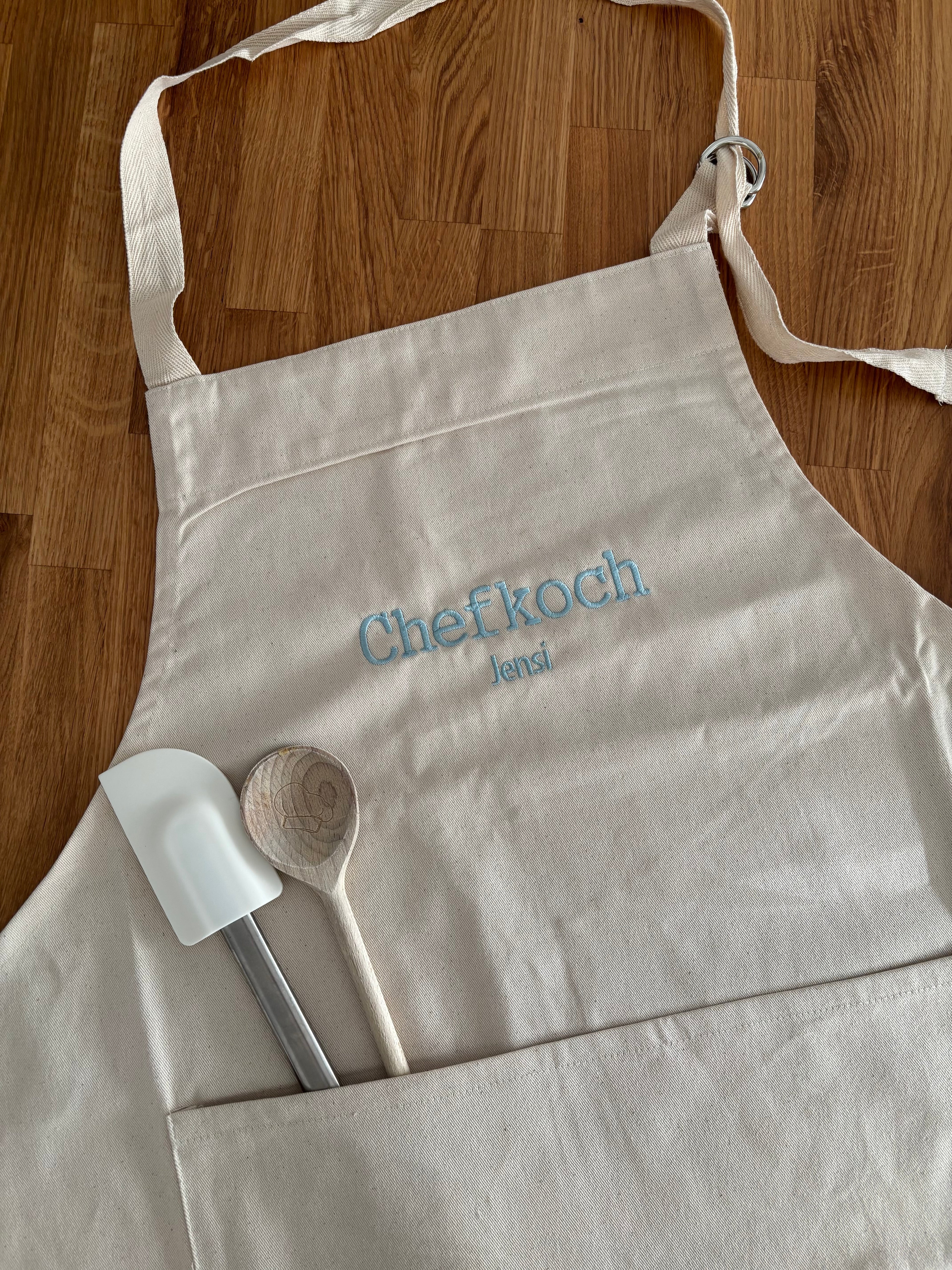 Eine Kochschürze für Erwachsene mit einer individuellen Stickerei in hellblau: Chefkoch Jensi.