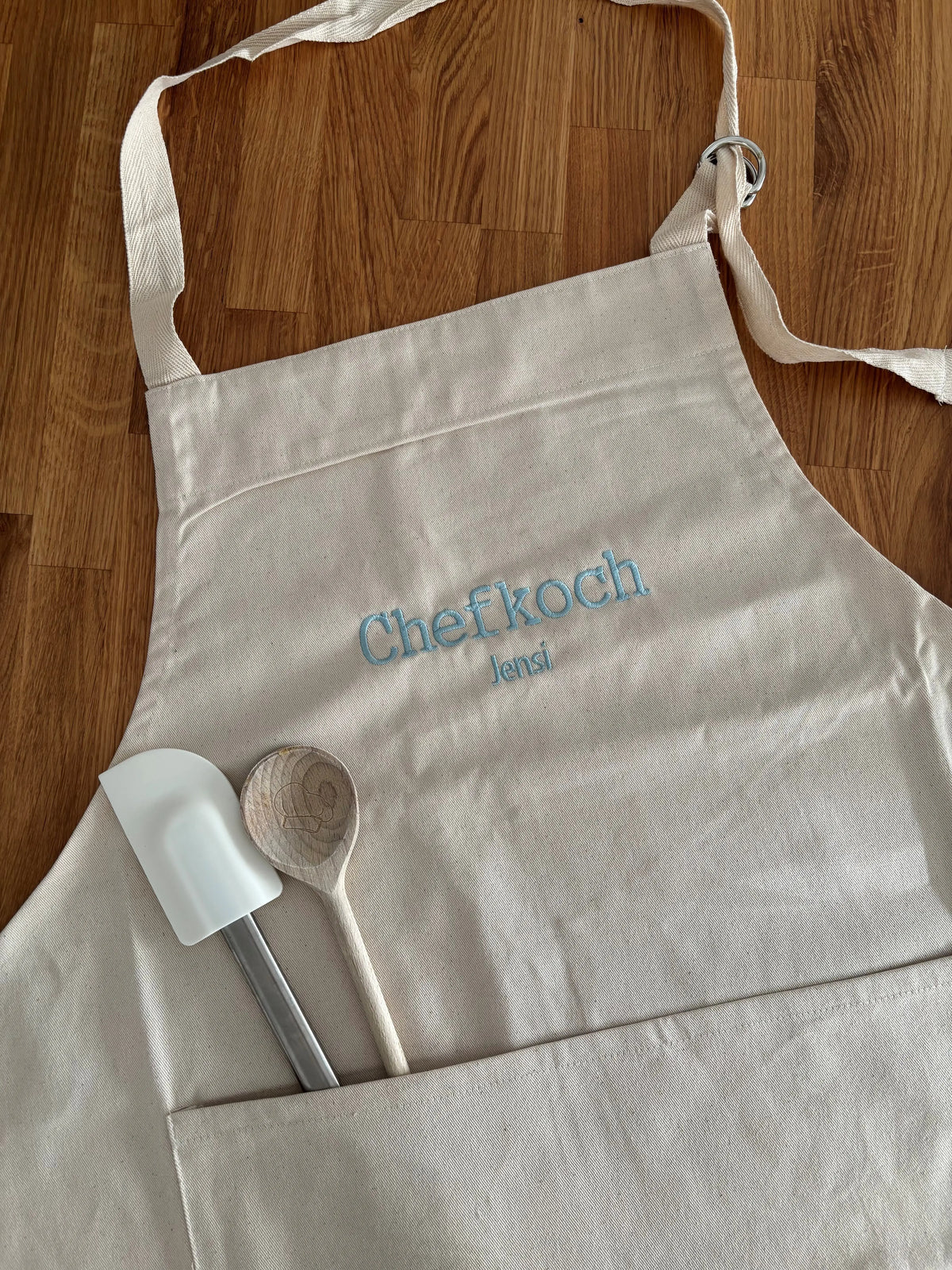Eine Kochschürze für Erwachsene mit einer individuellen Stickerei in hellblau: Chefkoch Jensi.