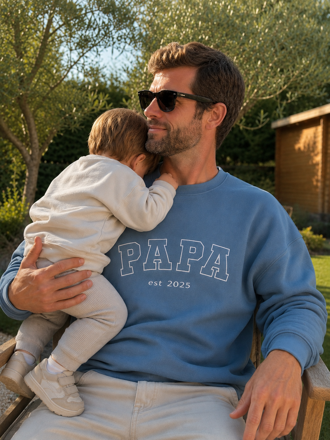 Ein Vater trägt ein personalisiertes Sweatshirt, wo vorne "PAPA est 2025" in weiß gestickt ist.