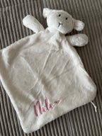 Ein Schmusetuch Lämmchen in weiß mit einer rosanen Stickerei an der Seite "Nele" mit einem Herz.