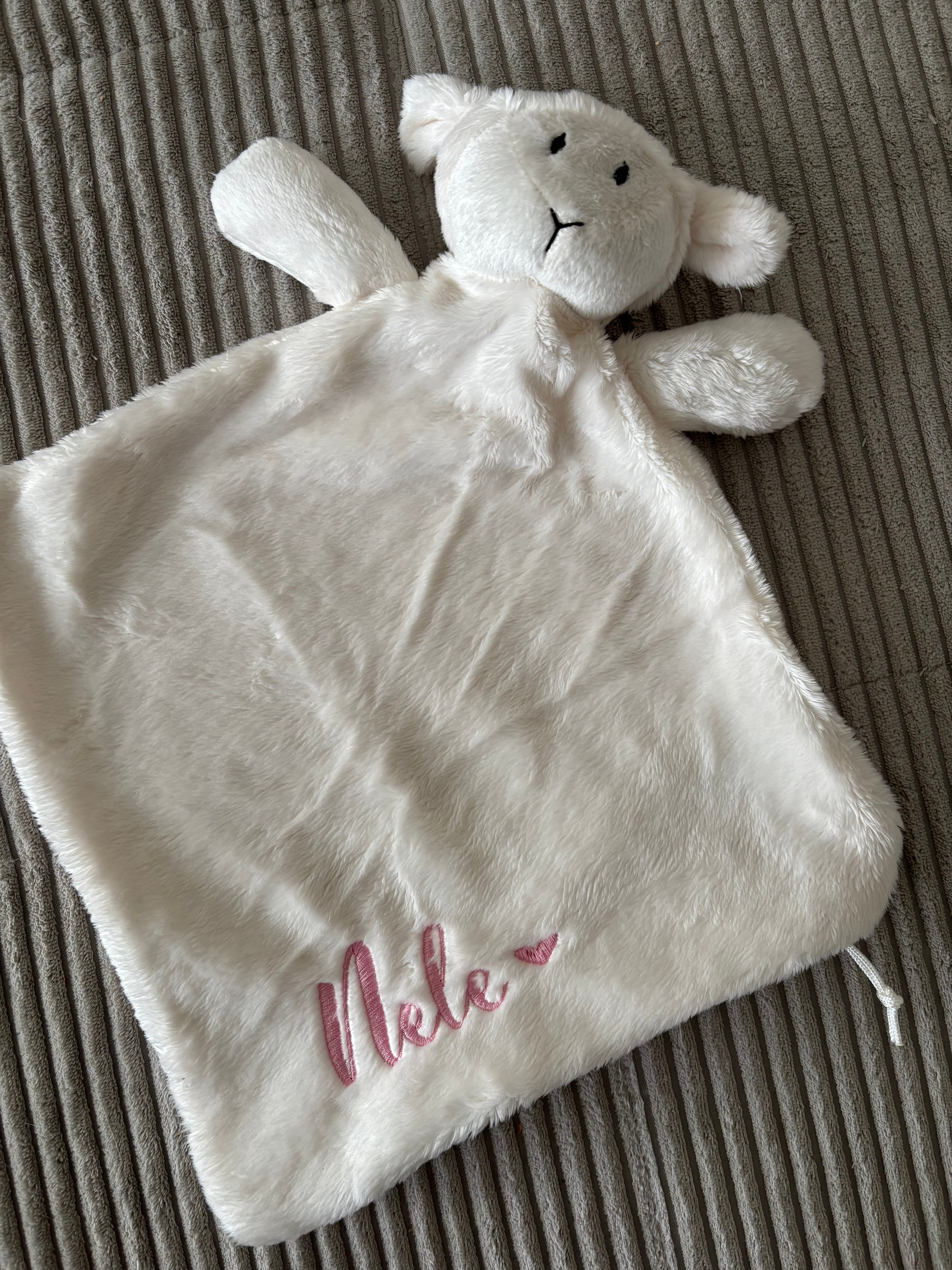 Ein Schmusetuch Lämmchen in weiß mit einer rosanen Stickerei an der Seite "Nele" mit einem Herz.