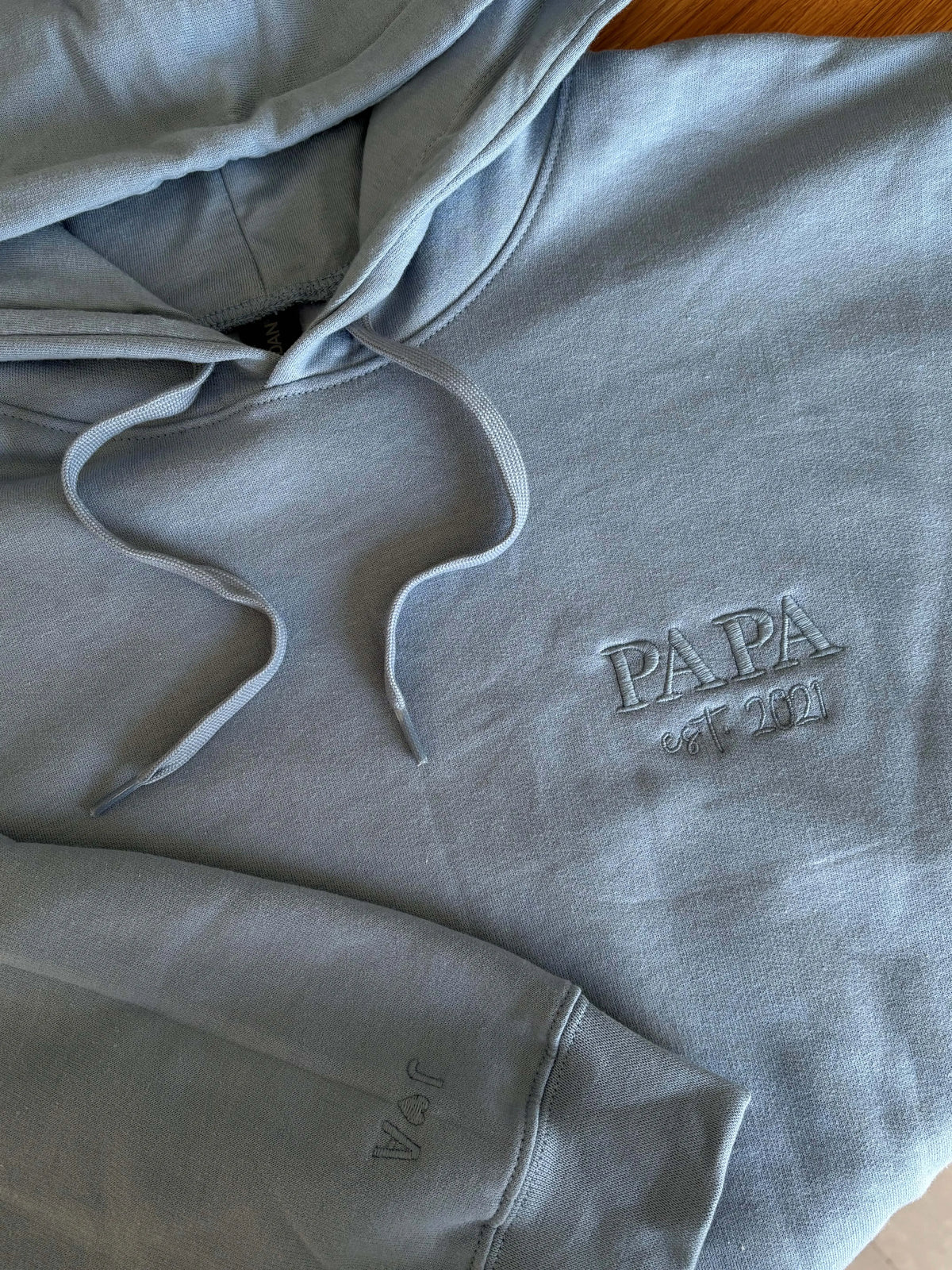 Ein Hoodie in der Farbe Light Blue mit einer Stickerei in der Farbe Light Blue: PAPA est. 2021.