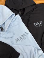 Zwei Hoodies in der Farbe Light Blue und Schwarz mit einem individuellen Wunschtext bestickt: Mama und Dad.