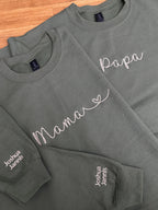 Zwei Sweater in der Farbe Military Greenfür Eltern. Beide sind jeweils mit Mama und Papa bestickt worden. Auf dem Ärmel tragen sie beide die Kindernamen Joshua und Jannis.