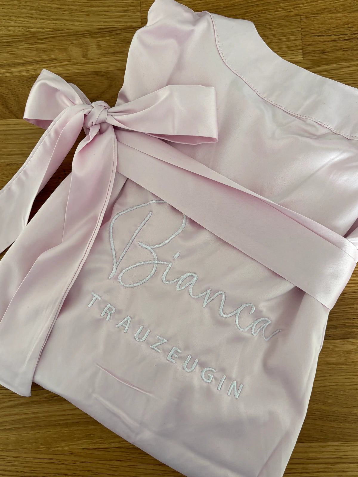 Ein rosa Morgenmantel mit einer weißen Stickerei hinten auf dem Rücken: Bianca Trauzeugin. 