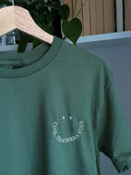 Ein T-Shirt in der Farbe Military Green mit einem beigen Stickerei vorne links auf der Brust „Cool Teachers Club" in Großbuchstaben.